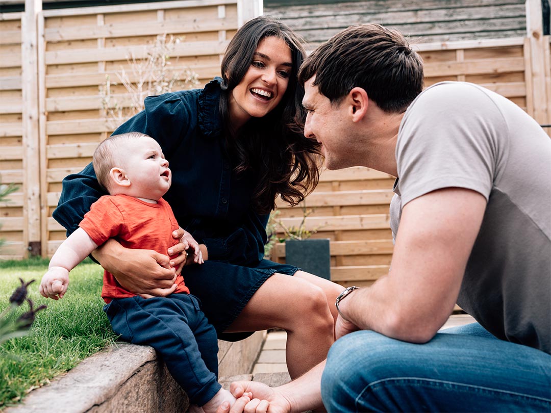 Man and woman sat in garden with baby