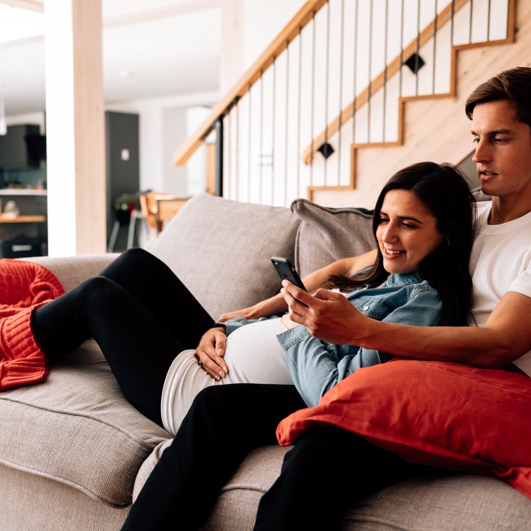 Pregnant woman and man lying on sofa looking at mobile phone