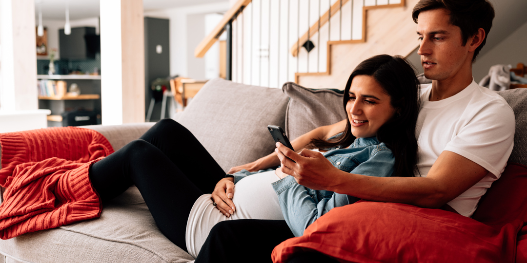 Pregnant woman and man lying on sofa looking at mobile phone
