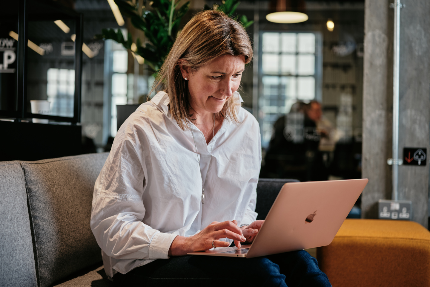 Woman sat on sofa in Work Cafe on laptop