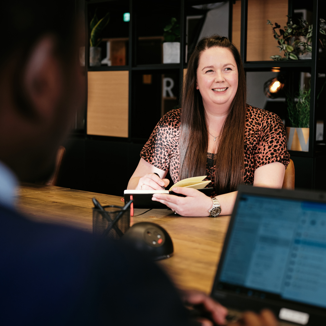 Woman sat at co-working desk in work cafe with notepad and pen