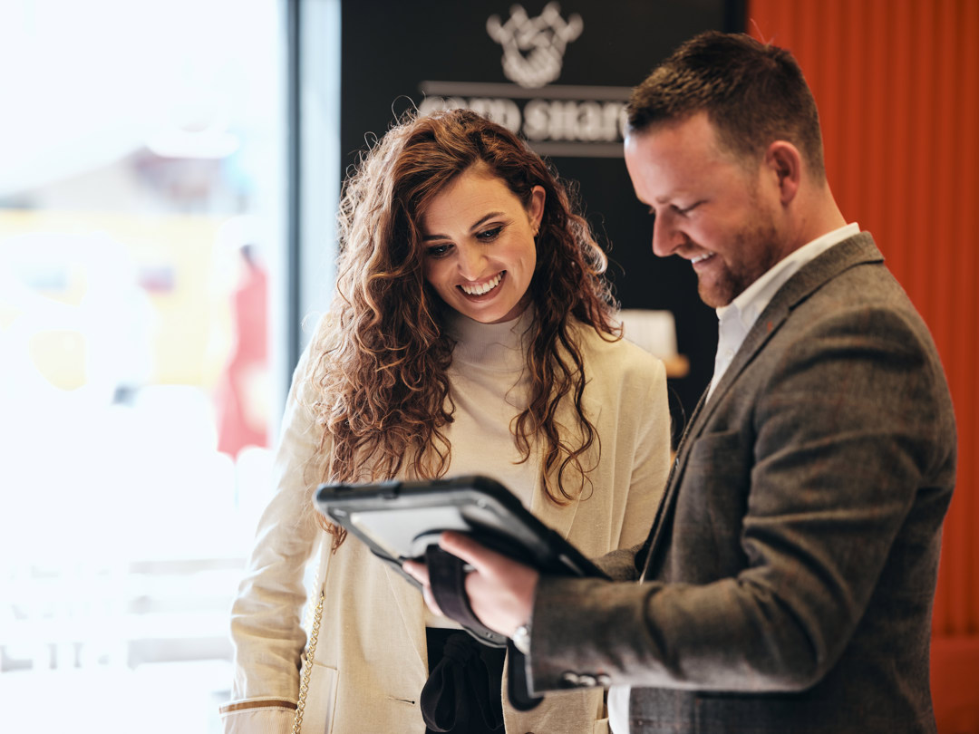 Man with iPad stood talking to woman in Work Cafe