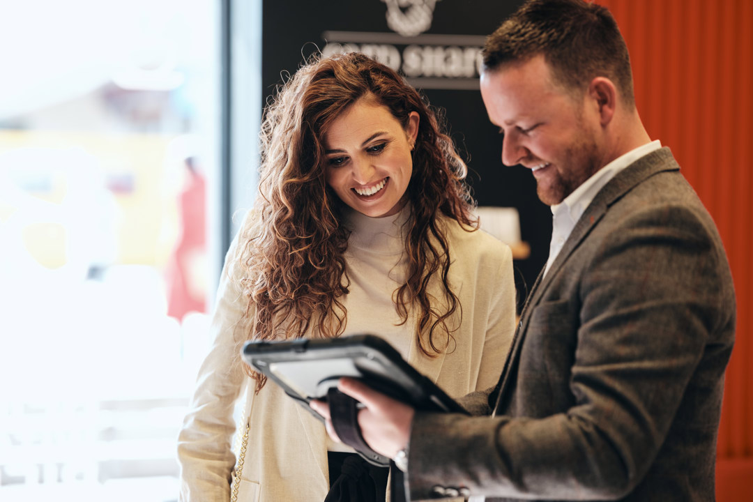 Man with iPad stood talking to woman in Work Cafe