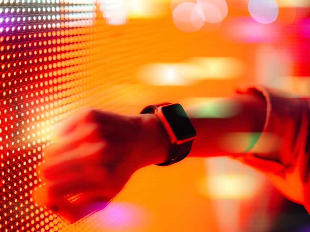 Close up shot of a woman using smart watch against colourful neon light display