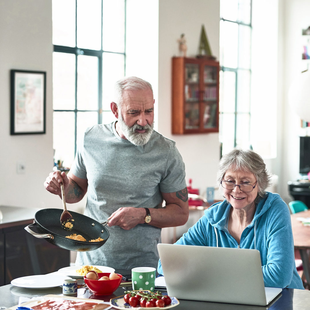 Man in kitchen cooking next to woman on lap top