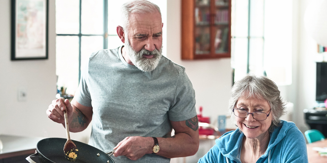Man in kitchen cooking next to woman on lap top